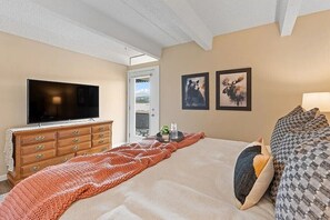 A bedroom with a TV, wooden dresser, bed with patterned bedding, and two wall art pieces. - Lake and Lift Retreat: Your All-Season Escape (Dillon)