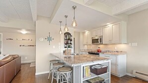 Una cucina con mobili bianchi, un'isola centrale con sgabelli e illuminazione a sospensione.