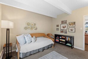 Ein Schlafzimmer mit Bett, Nachttisch, Lampe, Wandbild und Bücherregal.