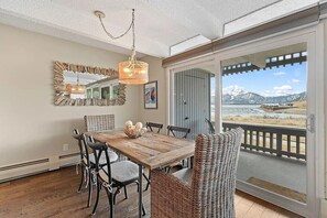 A dining area with a wooden table, wicker chairs, a chandelier, and a large window with a mountain view. - Lake and Lift Retreat: Your All-Season Escape (Dillon)