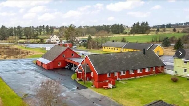 A rural setting with a red barn and a yellow building, surrounded by green fields and a few houses in the background.