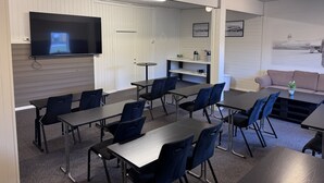 A conference room with a flat-screen TV, multiple tables and chairs, a small round table, and a sofa.