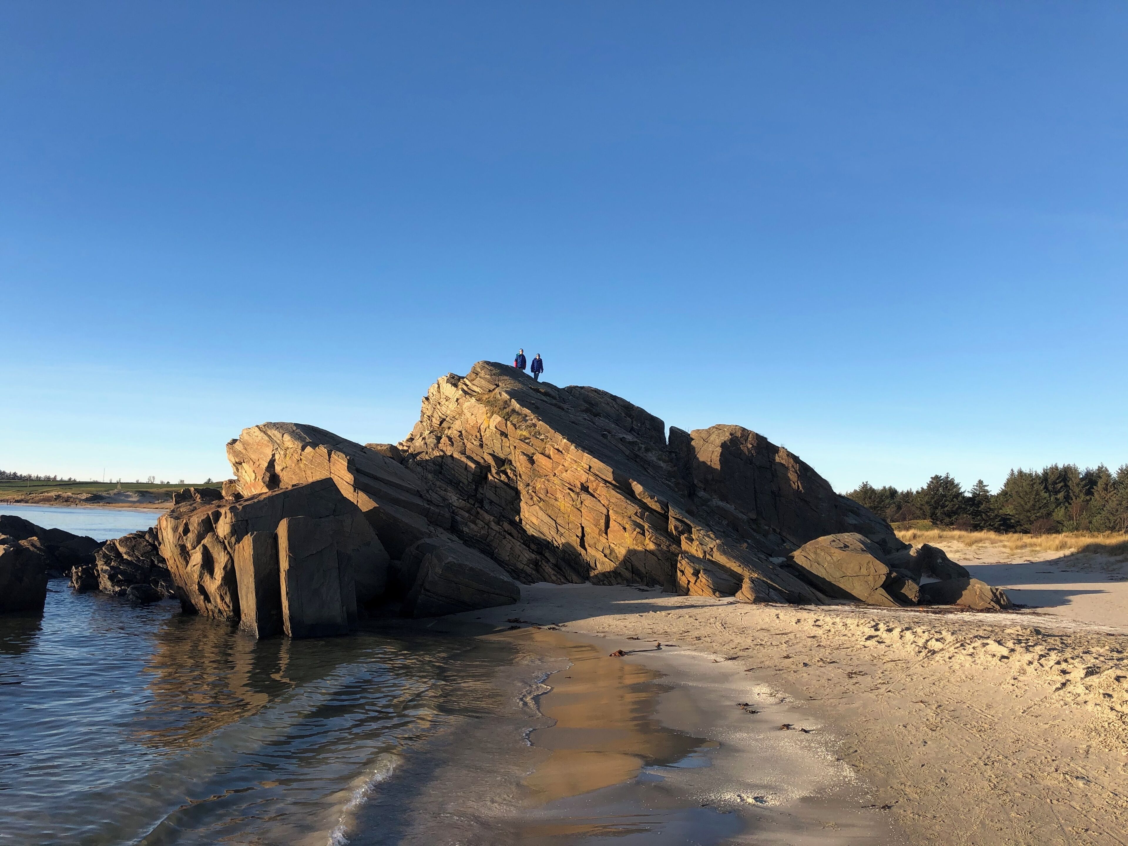 A rocky shoreline with two people standing on a large rock formation.