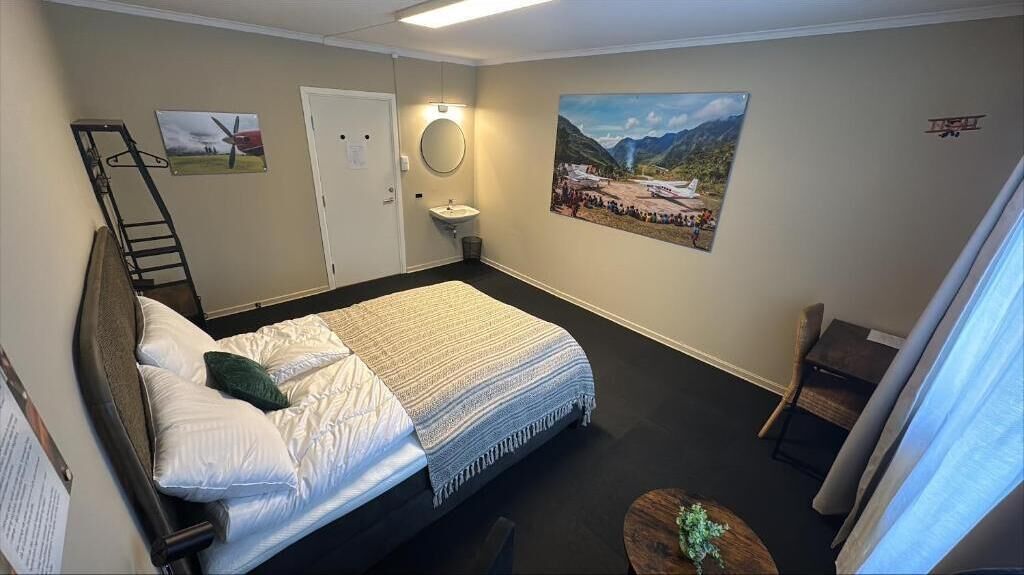 Une chambre à coucher avec un lit, un bureau, une chaise, une échelle, un lavabo et un tableau accroché au mur.