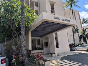 A hotel entrance with a covered walkway, palm trees, and a car parked in front. - Beachfront 4BR, 2 Condos for 12 in Kihei, Hawaii! (Kihei)