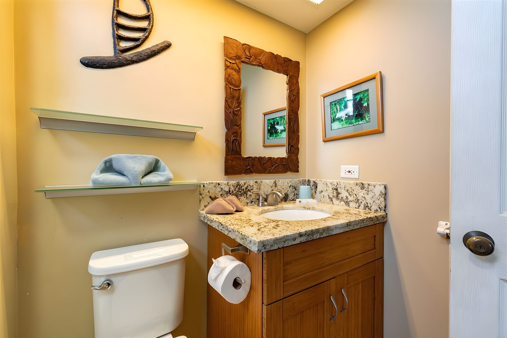 A bathroom with a toilet, sink, wooden cabinets, a mirror, and a shelf with towels.