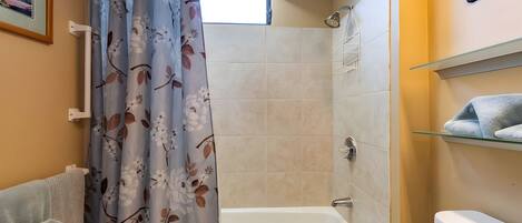 A bathroom with a shower, a bathtub, a toilet, and a shelf with towels.