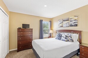 A bedroom with a bed, dresser, TV, artwork, and a window with curtains. - 7 Bedroom Villa Near Disney World – Pool & Spa, Kissimmee (Kissimmee)