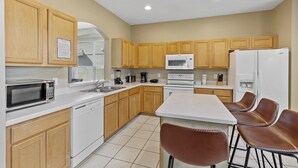 A kitchen with wooden cabinets, a microwave, a stove, a refrigerator, a sink, and a bar area with stools. - 7 Bedroom Villa Near Disney World – Pool & Spa, Kissimmee (Kissimmee)
