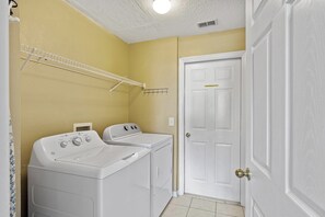 A laundry room with two white washers and dryers, a white door, and a yellow wall. - 7 Bedroom Villa Near Disney World – Pool & Spa, Kissimmee (Kissimmee)