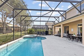 A covered outdoor swimming pool with a patio area, chairs, and a table. - 7 Bedroom Villa Near Disney World – Pool & Spa, Kissimmee (Kissimmee)