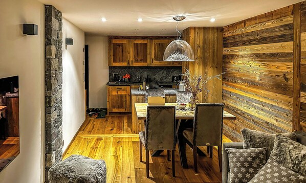 A modern kitchen with wooden cabinets, a dining table with chairs, and a pendant light. - Adorable 3-bedroom apartment in Val de Bagnes perfect for relaxing (Val de Bagnes)