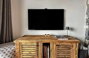 A room with a large flat-screen TV mounted on the wall, a wooden coffee table with books and decorative items, and a lamp on the table. - Adorable 3-bedroom apartment in Val de Bagnes perfect for relaxing (Val de Bagnes)