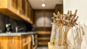 Une cuisine avec des meubles de rangement en bois, un vase en verre contenant des branches séchées et une ombre sur le mur.