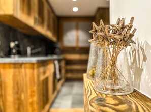 A kitchen with wooden cabinets, a glass vase with dried branches, and a shadow on the wall. - Adorable 3-bedroom apartment in Val de Bagnes perfect for relaxing (Val de Bagnes)