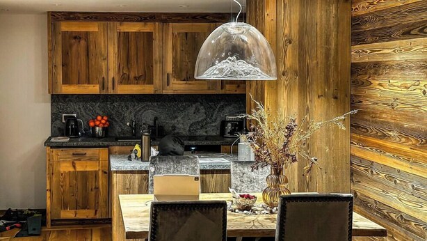 Une cuisine avec des meubles de rangement en bois, un plan de travail en marbre, une machine à café et une table à manger avec des chaises.