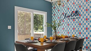 A dining area with a table set for six, a chandelier, and a wall with a chessboard pattern and the word 'Charlotte' on it. - New! Sleeps 20 — Hot Tub, Minigolf, Firepit,Outdoor Movie & Game Room (Charlotte)