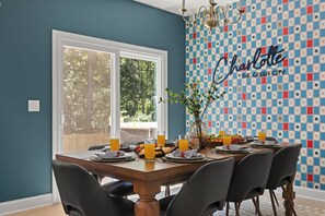 A dining area with a table set for six, a chandelier, and a wall with a chessboard pattern and the word 'Charlotte' on it. - New! Sleeps 20 — Hot Tub, Minigolf, Firepit,Outdoor Movie & Game Room (Charlotte)
