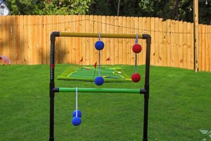 A golf putting practice setup with a green mat, a wooden fence, and a grassy lawn. - New! Sleeps 20 — Hot Tub, Minigolf, Firepit,Outdoor Movie & Game Room (Charlotte)
