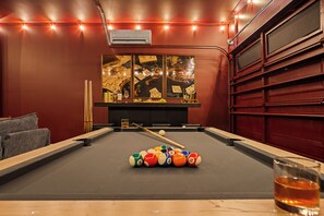 A pool table with balls, a glass of amber liquid, and a painting with playing cards. - New! Sleeps 20 — Hot Tub, Minigolf, Firepit,Outdoor Movie & Game Room (Charlotte)
