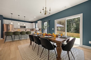 A modern kitchen with white cabinets, a stainless steel refrigerator, and a dining area with a wooden table and black chairs. - New! Sleeps 20 — Hot Tub, Minigolf, Firepit,Outdoor Movie & Game Room (Charlotte)