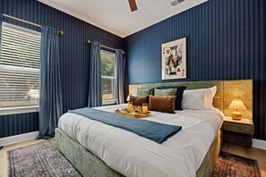 Une chambre à coucher avec un grand lit, une table de chevet, une lampe, un tableau et une fenêtre avec des rideaux.