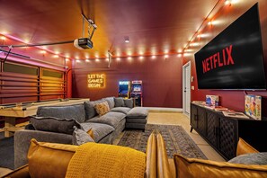 A cozy living room with a pool table, a large flat-screen TV, and a neon sign that reads 'LET THE GAMES BEGIN.' - New! Sleeps 20 — Hot Tub, Minigolf, Firepit,Outdoor Movie & Game Room (Charlotte)