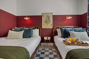 A hotel room with two beds, a small round table, a checkered rug, and a breakfast tray with croissants and fruit. - New! Sleeps 20 — Hot Tub, Minigolf, Firepit,Outdoor Movie & Game Room (Charlotte)