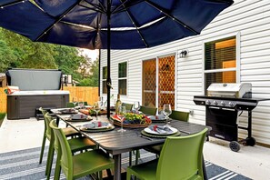 Une terrasse extérieure avec une table à manger pour quatre personnes, entourée de chaises vertes, sous un grand parasol.