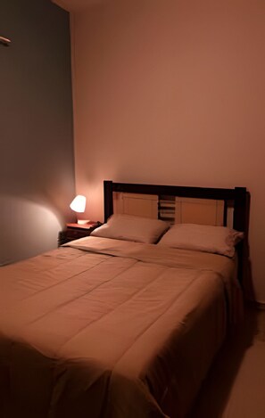 A single bed with a wooden headboard, a bedside table with a lamp, and a plain wall.
