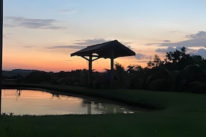 A gazebo structure near a body of water with a sunset in the background. - SHB Chácara para Eventos com Piscina (Elias Fausto)