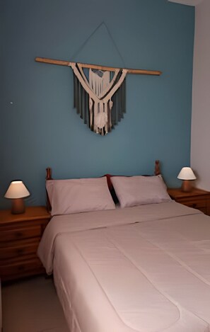 Een slaapkamer met een bed, twee nachtkastjes, een macramé wanddecoratie en twee lampen.