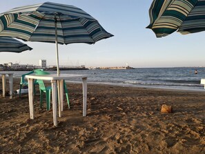 Une plage avec des parasols à rayures, une table avec des chaises et une côte rocheuse.