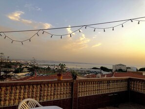 Un balcon avec vue sur la mer, une plante en pot et une guirlande lumineuse.