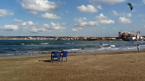 A beach with a view of the sea, a building with construction cranes, and a person flying a kite. - Stunning Beachfront Apartment Just 3 Minutes from Sidi Fredj Beach (Staoueli)
