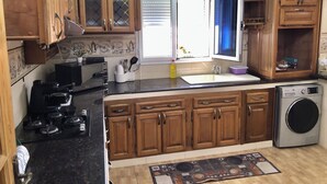 A kitchen with wooden cabinets, a built-in washing machine, and a window with blinds. - Stunning Beachfront Apartment Just 3 Minutes from Sidi Fredj Beach (Staoueli)