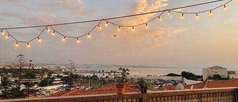 A terrace with a view of the sea, string lights, and a brick balustrade.