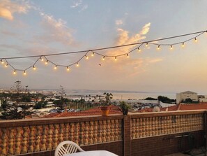 Een terras met uitzicht op zee, met lichtjes en een bakstenen balustrade.