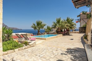 Ein Poolbereich mit Liegestühlen, einem Steinboden und Blick aufs Meer.