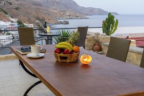 A table with a fruit basket, a cup, and a lit candle, overlooking a coastal landscape with buildings and a cactus. - Aeriko Villa with Private pool - Where mountains meet the sea (Heraklion)