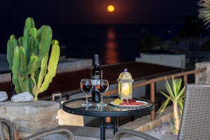 Ein Tisch mit einer Flasche, Gläsern und Obst, vor einer Sonnenuntergangsszene.