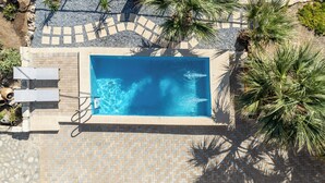 A rectangular swimming pool with a tiled border, surrounded by a pebble walkway and palm trees. - Aeriko Villa with Private pool - Where mountains meet the sea (Heraklion)