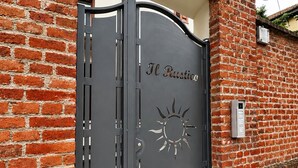 Ein Metallgitter mit der Aufschrift 'Il Rustico' und einem Sonnendesign vor einer Ziegelwand.