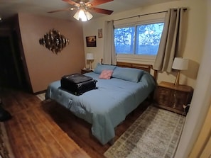 A bedroom with a bed, a suitcase, a ceiling fan, a window with curtains, and a nightstand with a lamp. - Tranquil 3 BDR family friendly home. 10min to town. 20min to Pajarito Ski Hill. (Los Alamos)
