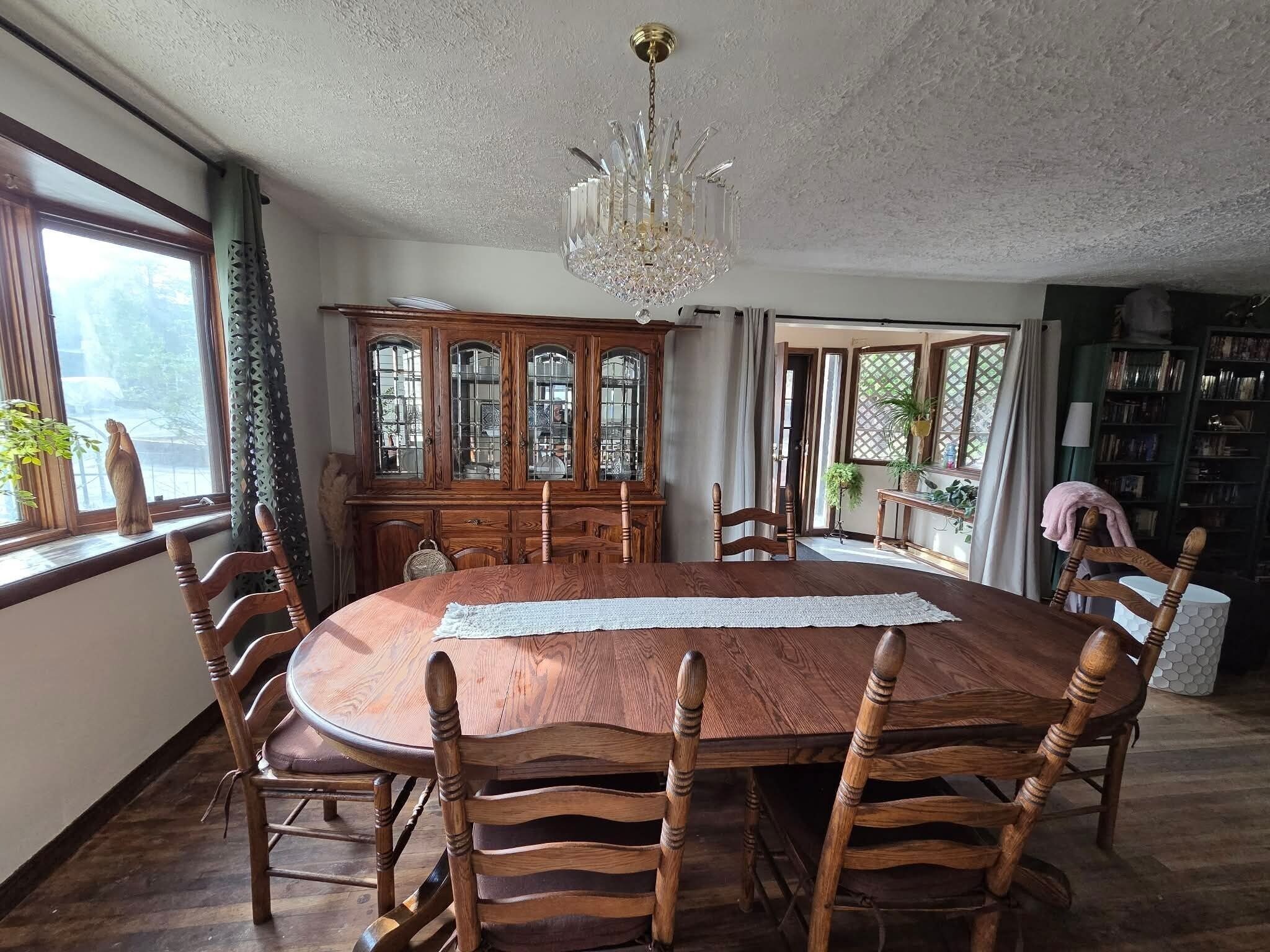 Une salle à manger avec une table ronde en bois, six chaises, un buffet en bois et un lustre.