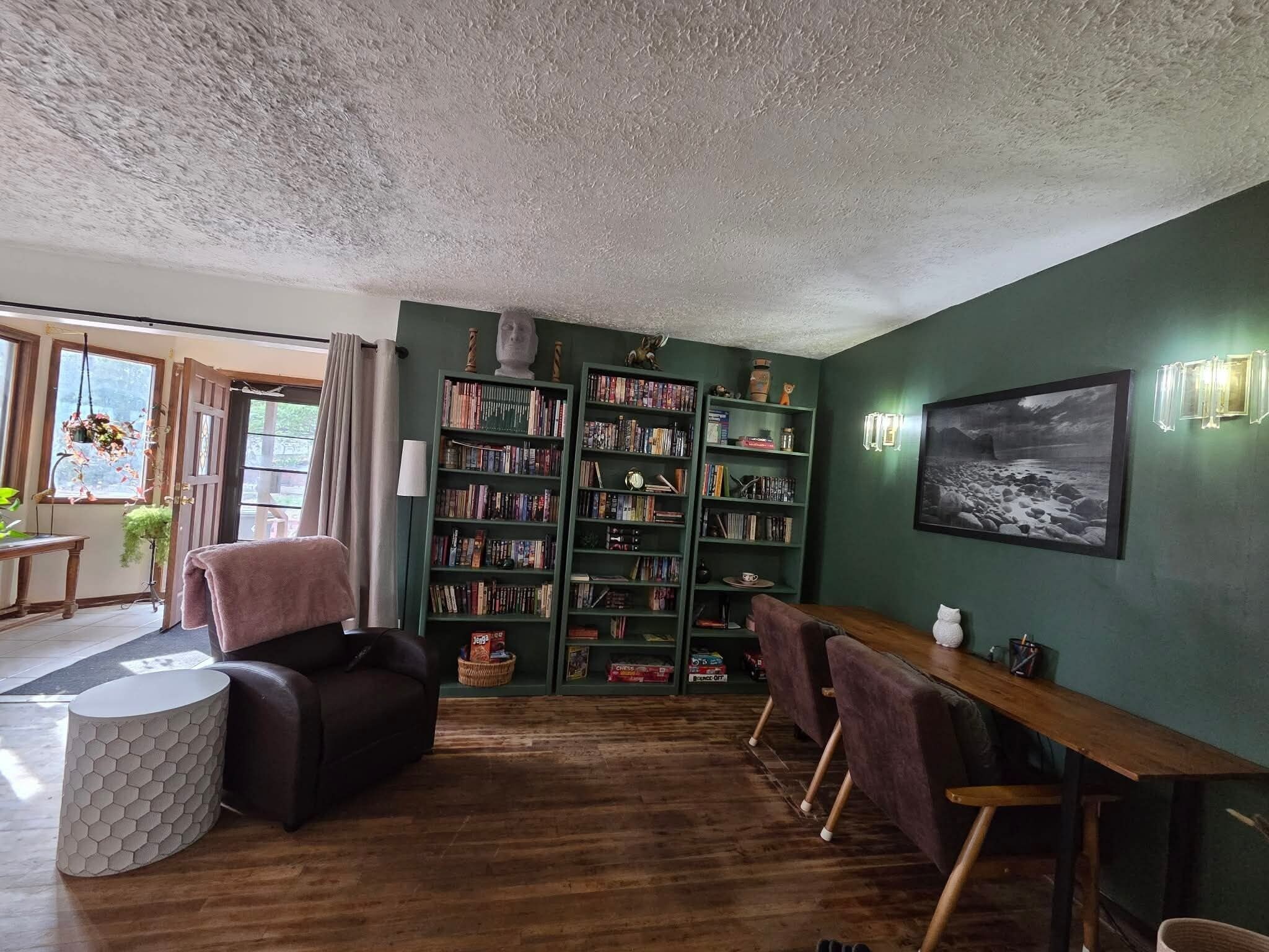A cozy living room with a wooden floor, a sofa, a dining table with chairs, and a bookshelf filled with books.