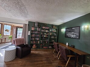 Ein gemütliches Wohnzimmer mit Holzboden, einer Couch, einem Esstisch mit Stühlen und einer Bücherwand voller Bücher.