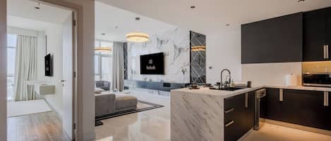 A modern kitchen with a marble island, dark cabinetry, and a flat-screen TV.