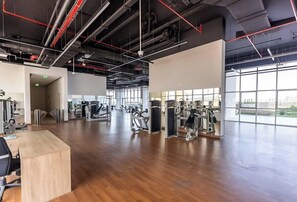 A spacious gym with various exercise equipment, large windows, and a wooden floor. - Premium 1BR w/ Balcony | Mins to Marina & Metro (Dubai)