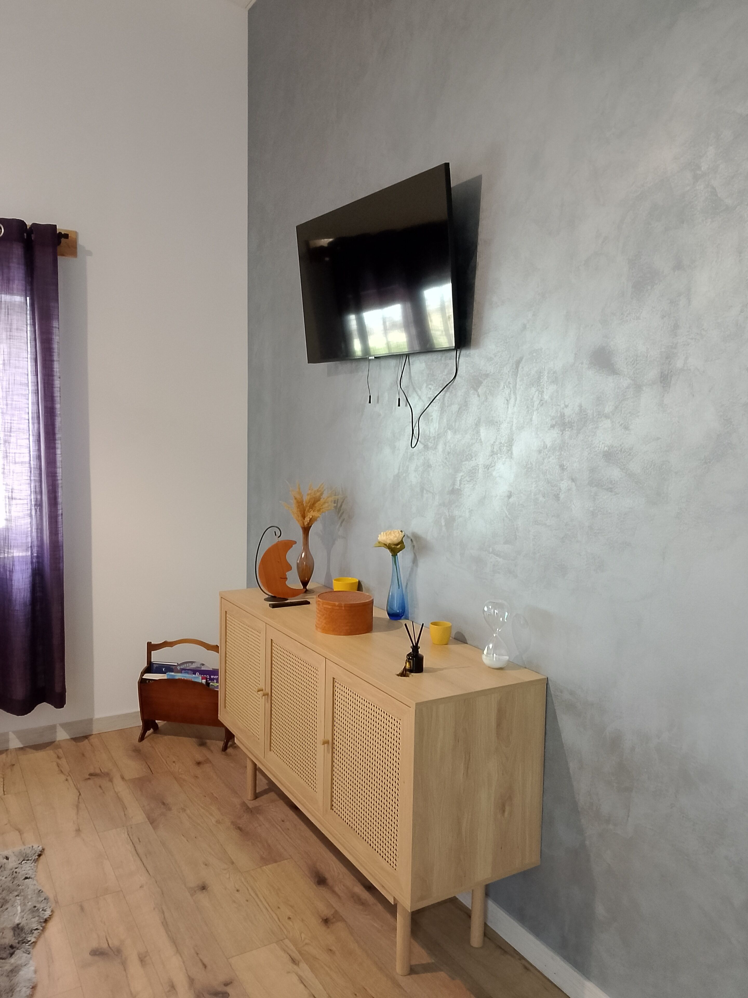 Una habitación con un armario de madera, un televisor montado y una estantería.